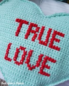 a crocheted heart with the words true love written on it in red and blue