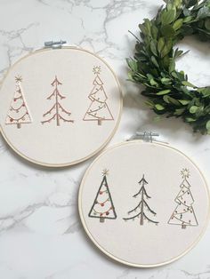 two cross stitch christmas trees sitting on top of a white counter next to a wreath