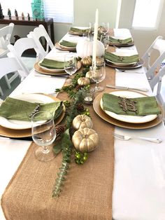 the table is set with white and gold plates, green napkins, silver pumpkins and greenery