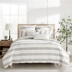 a bed with white and grey striped comforter next to a tree in a room