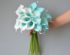 a person holding a bouquet of flowers on a gray background with white and blue petals