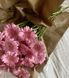 a bunch of pink flowers sitting on top of a white table next to brown paper