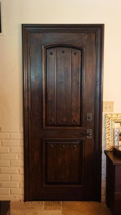 a brown wooden door sitting next to a white brick wall with a mirror on it