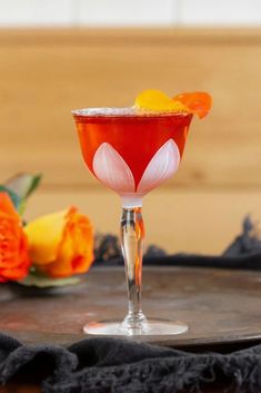 an orange and red drink sitting on top of a wooden table next to some flowers