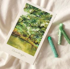 two crayons are sitting next to a card with a painting of a tree