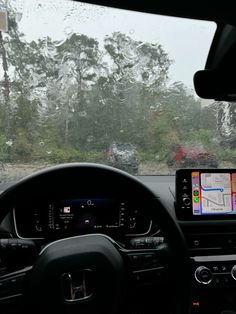 the dashboard of a car on a rainy day with trees in the backgroud