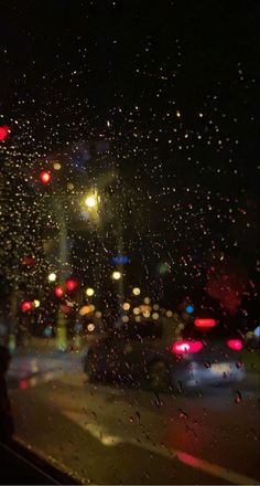 rain is falling down on the windshield of a car as traffic lights shine in the background