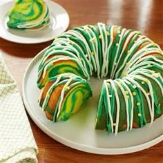 a bundt cake with green and white icing on a plate next to a napkin