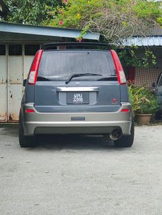 the back end of a gray car parked in front of a house with trees and bushes