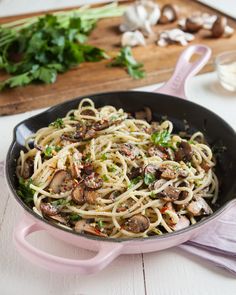 a pan filled with pasta and mushrooms on top of a wooden cutting board next to parsley