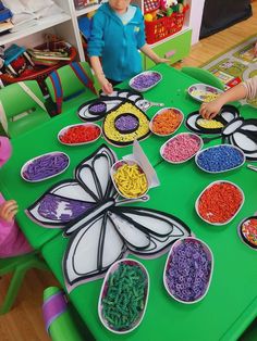 two children sitting at a green table with paper plates filled with cereals and candy