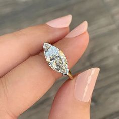 a woman's hand holding an engagement ring with a pear shaped diamond in it