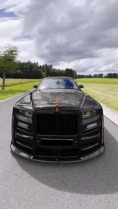 a black sports car driving down a road next to a lush green field on a cloudy day