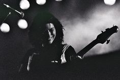 black and white photograph of a woman playing an electric guitar on stage with lights in the background