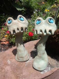 two ceramic sculptures with blue eyes on top of a rock in front of some flowers