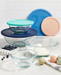 several bowls with eggs, flour and blueberries on a counter top in front of white tiles