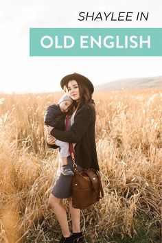 a woman holding a baby in her arms while standing next to a tall grass field