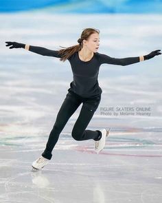 a woman skating on an ice rink with her arms out and one hand in the air