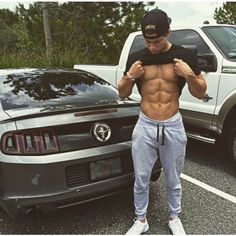 a man standing in front of a car with his shirt off and no shirt on