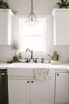 a kitchen with white cabinets and black faucet, potted plants on the window sill