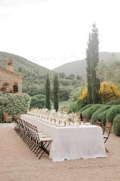 an outdoor dining table set up with white linens and gold place settings, surrounded by greenery