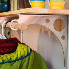 a rack with two yellow bowls on top of it next to a green shirt and red jacket