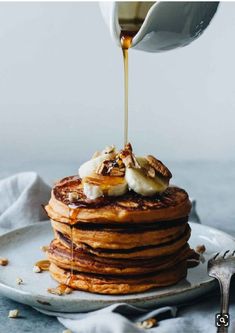 a stack of pancakes being drizzled with maple syrup and topped with bananas