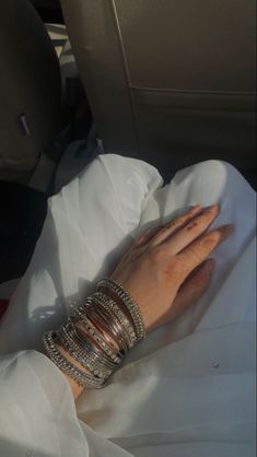 a woman's hand with bracelets and rings on her arm in the back seat of a car