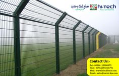 a green fence next to a dirt road and grassy field on a foggy day