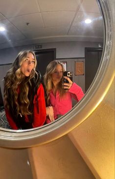 two women standing in front of a mirror taking a selfie