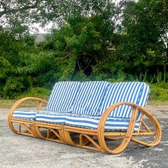 a wicker couch with blue and white striped cushions in front of some trees,