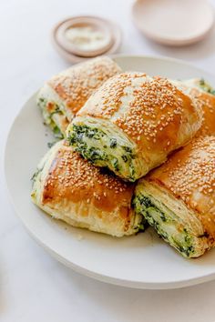 rolls with cheese and spinach are on a white plate next to dipping sauces