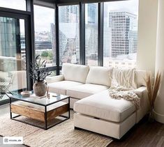 a living room filled with furniture and large windows overlooking the cityscape in the background