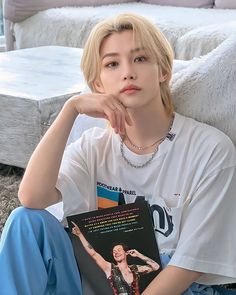 a person sitting on the ground with a book in their hand and wearing a white shirt