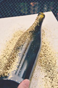 a person is holding a bottle with gold flakes on it and there is a knife in front of the bottle