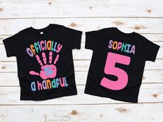 two black shirts with pink and blue handprints on them, one has the number five