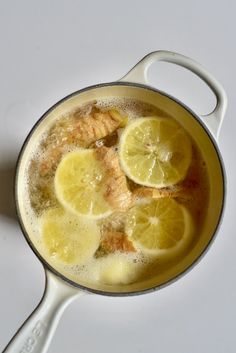 a pan filled with lemons and water on top of a white counter next to a spoon