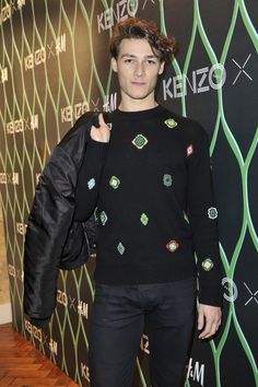 a young man standing in front of a wall with an embellishment on it