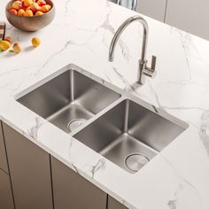 two stainless steel sinks in a kitchen with marble counter tops and white cabinets next to a bowl of fruit