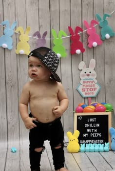 a baby boy wearing a hat standing in front of some bunnies and bunny decorations