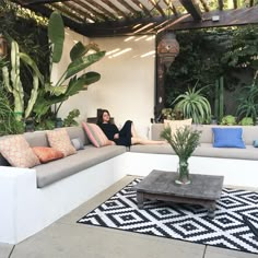 a woman sitting on a couch in the middle of a patio with potted plants