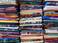 many different colored fabrics are stacked on top of each other in this photo, there is a pile of them