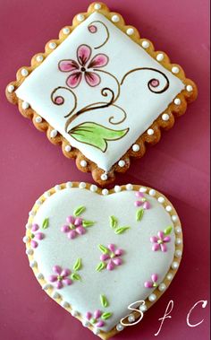 two decorated heart shaped cookies on a pink surface