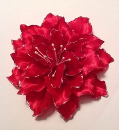 a red flower with pearls on it sitting on top of a white table next to a wall