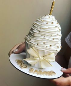 a person holding a cake shaped like a cupcake with gold and white decorations on it