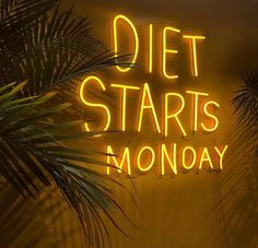 a neon sign that says diet starts monday on the side of a wall next to palm trees