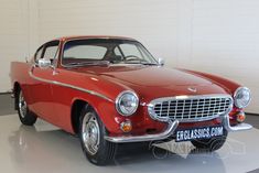 an old red car is parked in a white room with a sign on the wall