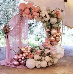 an arch made out of balloons and flowers on top of a floor under a tent