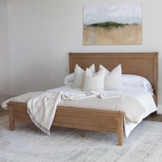 a bed with white pillows and blankets on top of it in a bedroom next to a painting