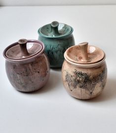 three ceramic containers sitting on top of a white table